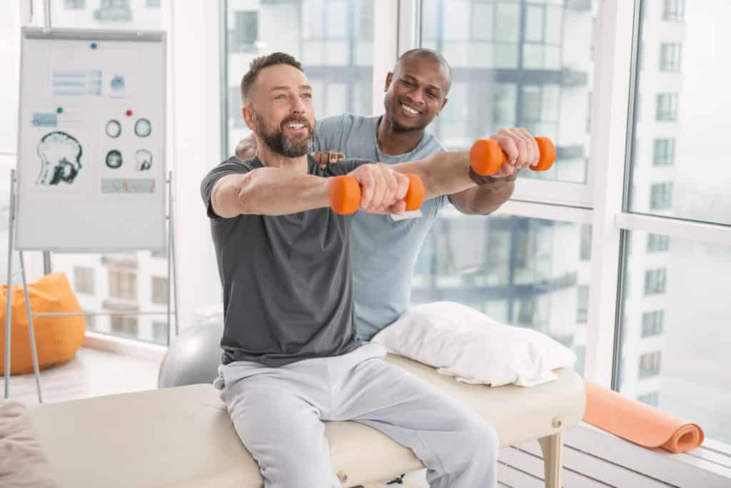 Joyful positive man lifting dumbbells in front of him while enjoying this exercise