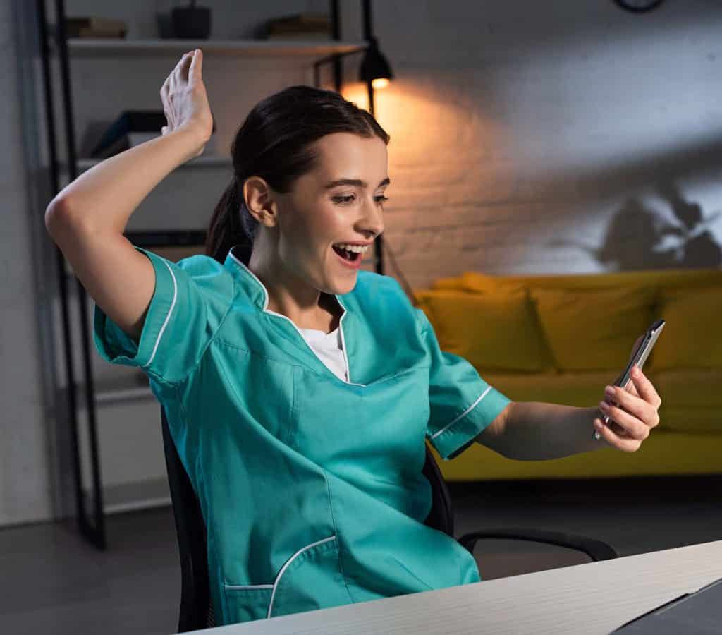 Nurse in scrubs looking excited at news on her phone.