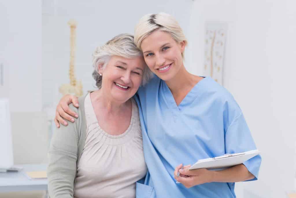 Friendly nurse with arm around senior patient in clinic